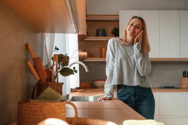 Ayakta dikilip telefonla konuşuyor. Güzel genç bayan mutfakta..