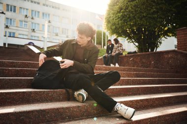 Adam merdivenlerde oturuyor. Gündelik giysiler içindeki genç öğrenciler açık havada birlikteler..