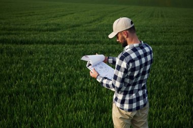 Bekliyor, belgeyi tutuyor. Başlık olarak. Yakışıklı genç adam tarım alanında..