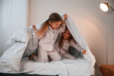 Battaniyeyi tutuyorum. İki küçük kız evcil odada oynuyorlar ve eğleniyorlar..