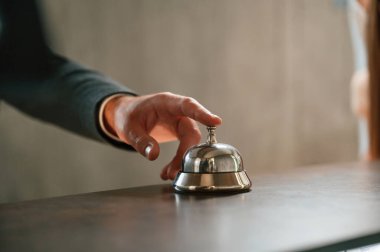 Otel masasının zilini kullanarak manzarayı kapat. Otel resepsiyonunda siyah ceketli bir adam var..