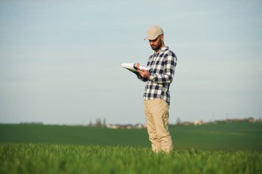İşçi belgeyi okuyor. Yakışıklı genç adam tarım alanında..