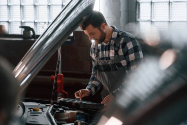 Arabanın kaputu açıldı. Tablet kullanıyorum. Üniformalı adam araba galerisinde çalışıyor..