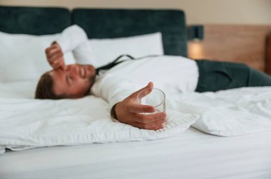 Elindeki boş bardak, yatağa uzanmış, yorgun. İş adamı içeride, otel odasında..