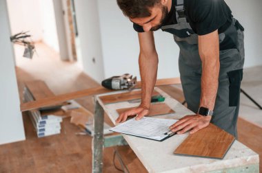 Bilgiyi okuyorum. Adam yeni kaplamalı ahşap döşeme kuruyor..