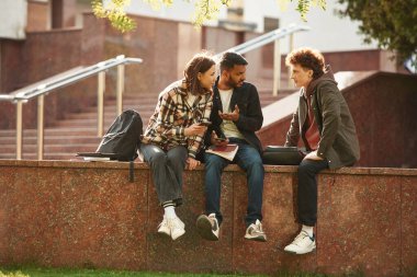 Gündelik giysiler içinde üç genç dışarıda beraberler..