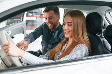 Otomobilin kontrollerini gösteriyor, oturuyor. Resmi elbiseli adam elektrikli arabalı kadın müşteriyle birlikte..