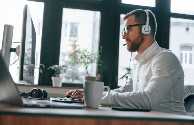 Çağrı merkezinde. Kulaklık takıyordu. Resmi kıyafetli bir ofis çalışanı bilgisayar başında oturuyor ve çalışıyor..