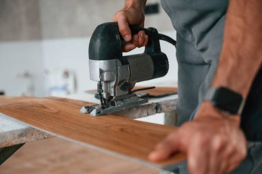 Tahtayı kesmek için elektrikli makineyi kullanmak. Adam yeni kaplamalı ahşap döşeme kuruyor..