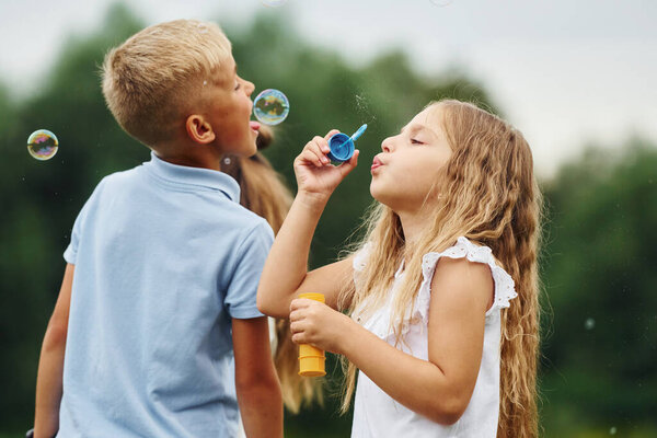 With bubbles. Kids are having fun on the field at daytime together.