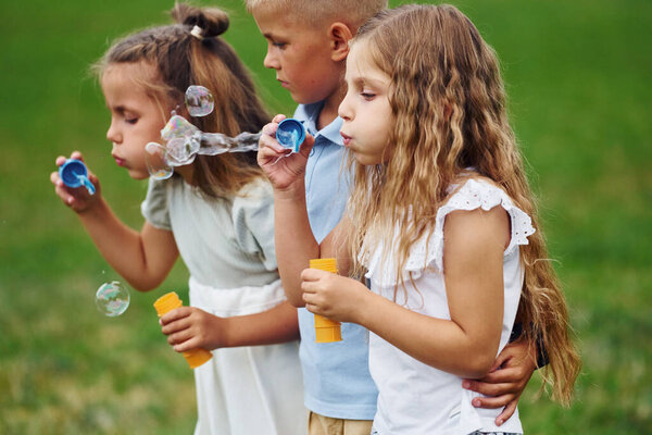 With bubbles. Kids are having fun on the field at daytime together.