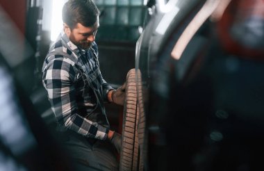 Yeni lastikleri tutuyor ve değiştiriyor. Üniformalı adam araba galerisinde çalışıyor..