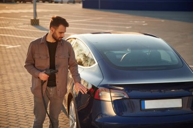 Otomobilin arka görüntüsü. Adam dışarıda elektrikli arabasının yanında duruyor..