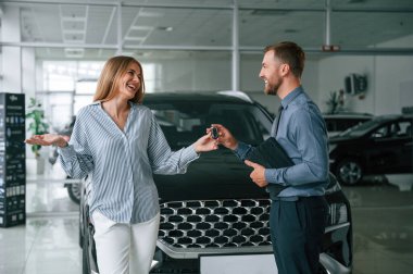 Otomobili almak, anahtarları almak. Resmi elbiseli adam elektrikli arabalı kadın müşteriyle birlikte..