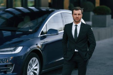 Ayakta, siyah takım elbiseli. İş adamı arabasının yanında..