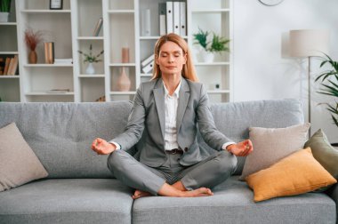Lotus pozu, meditasyon. Resmi elbiseli kadın evde, kanepede oturuyor..