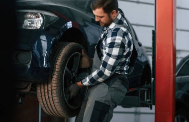 Yeni lastikleri tutuyor ve değiştiriyor. Üniformalı adam araba galerisinde çalışıyor..