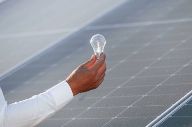 Yeşil enerji kavramı. Güneş panelinin önünde ışık topuzunu tutan insanın elini yakından görebilmek için..