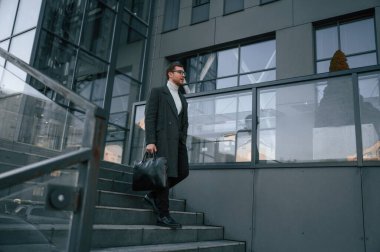 Çantayı tutuyorum. Resmi kıyafetli yakışıklı dışarıda, iş binasının yanında..