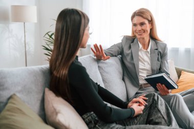 İki kadın kanepede oturuyor ve konuşuyor. Sıradan ve resmi kıyafetler..