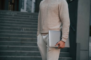 Merdivenlere karşı duran ve dizüstü bilgisayarını tutan adamın yakın görüntüsü..