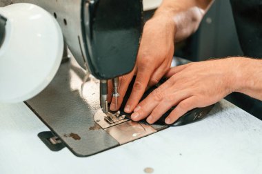 Dikiş işlemi. Manzarayı kapat. Sabit makine kullanan bir adamın elleri masanın üstünde..