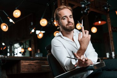 Ayakta ve elinde makasla. Yakışıklı berber kuaförde..