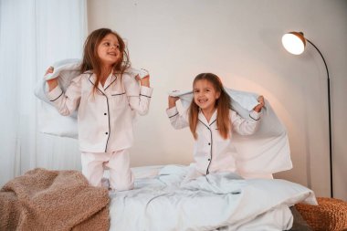 Yastıkları elinde tutarak. İki küçük kız evcil odada oynuyorlar ve eğleniyorlar..