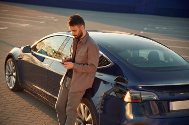 Güzel sarı güneş ışığı. Adam dışarıda elektrikli arabasının yanında duruyor..