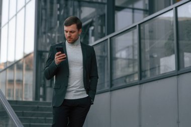 Resmi kıyafetler içinde akıllı telefon kullanan yakışıklı adamın arkasındaki pencereler..