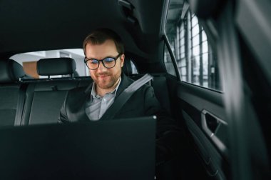 Dizüstü bilgisayarla, çalışıyor. Resmi iş elbiseli adam modern otomobilde oturuyor..