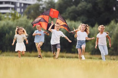 Birlikte koşmak. Bir grup çocuk koşuyor ve yeşil alanda uçurtmayla oynuyorlar..