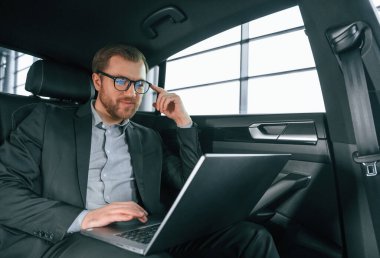 Dizüstü bilgisayarla, çalışıyor. Resmi iş elbiseli adam modern otomobilde oturuyor..