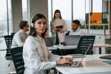 Kadın dizüstü bilgisayarla çalışıyor. Ofiste birlikte çalışan dört kişi var..