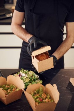 Kutuyu hamburgerle açıyorum. Adam yiyecek topluyor. İçeride, restoranda..