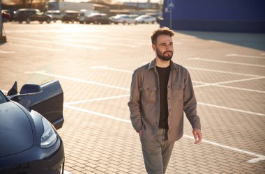 Ön manzara. Adam dışarıda elektrikli arabasının yanında duruyor..