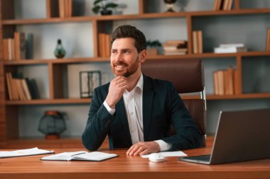 Masada dizüstü bilgisayarla oturuyor. Resmi kıyafetli bir iş adamı içeride çalışıyor..