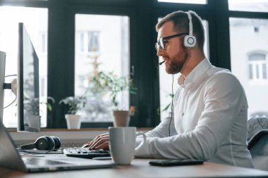 Çağrı merkezinde. Kulaklık takıyordu. Resmi kıyafetli bir ofis çalışanı bilgisayar başında oturuyor ve çalışıyor..