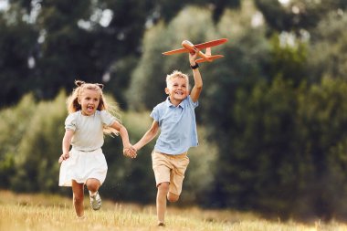 El ele tutuşarak. Erkek ve kız yeşil alanda oyuncak uçakla oynuyorlar..