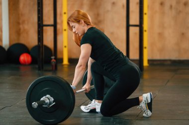 Yandan bak. Halterle yerde oturuyor. Güzel, güçlü kadın spor salonunda..