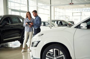 Güzel beyaz bir otomobil. Resmi elbiseli adam elektrikli arabalı kadın müşteriyle birlikte..