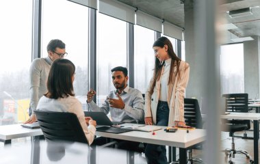 Masanın yanında. Ofiste birlikte çalışan dört kişi var..