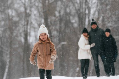 Kız, ailesinin ve erkek kardeşinin önünde duruyor. Mutlu aile dışarıda, kışın birlikte kar tatilinin tadını çıkarıyorlar..