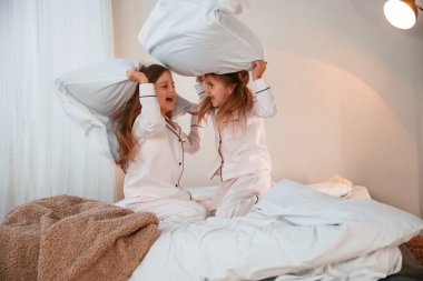 Yatakta. Yastık savaşı. İki küçük kız evcil odada oynuyorlar ve eğleniyorlar..