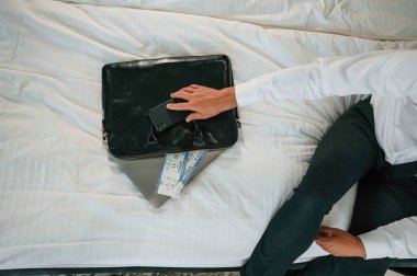 Yatakta oturan iş adamının yakın görüntüsü üzerinde seyahat biletleri var..