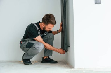 Tesisatçı, yeni yapılmış bir evin boş odasına ısıtma radyatörü yerleştiriyor..