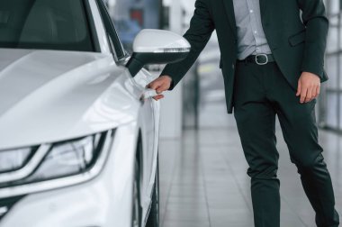 Yeni beyaz renkli otomobilin kapısını açan takım elbiseli adamın yakın görüntüsü.