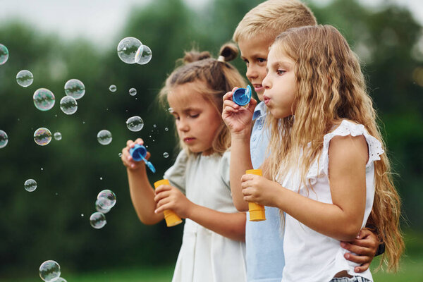 With bubbles. Kids are having fun on the field at daytime together.