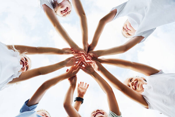 Вид снизу на детей, которые держатся за руки. На белом небе.