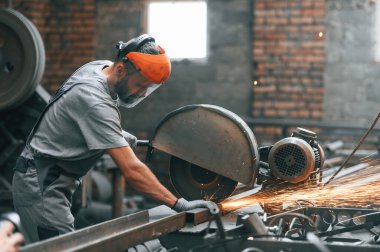 Yan görünüş, metali kesmek. Gri üniformalı genç fabrika işçisi.